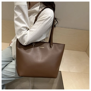 Detail of dark brown tote bag featuring golden metal logo and circular ring hardware