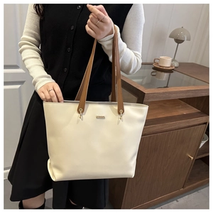 Detail of minimalist cream tote bag with brown handles and gold logo shown in lifestyle setting