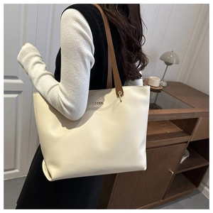 Minimalist cream leather tote bag with brown straps shown in a cozy interior setting
