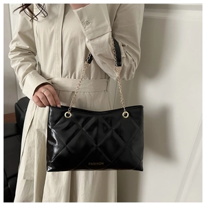 Détail d'un sac cabas matelassé noir avec chaîne dorée et logo FASHION sur un manteau beige