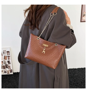 Detail view of woven brown tote bag with gold chain strap and deer pendant on model