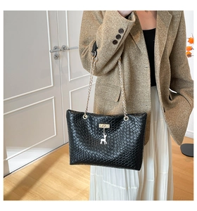 Detail of woven texture black bucket bag with golden chain and deer pendant charm