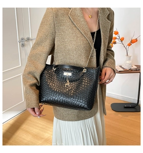 Detail of black woven bucket bag featuring gold deer charm and elegant chain strap