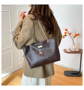 Close-up of deep brown woven tote bag featuring gold chain strap and deer charm detail