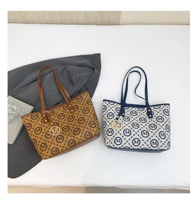 Détail de sacs fourre-tout imprimés avec motifs M et breloques dorées sur un bureau