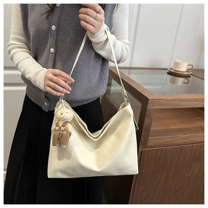 Cream tote bag with cute bear charm and fashion pendant in a warm lifestyle setting