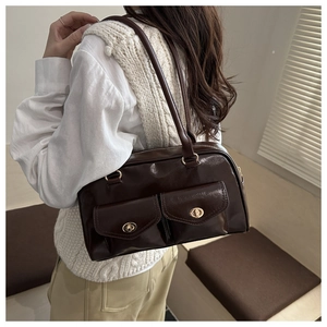 Detailansicht einer dunkelbraunen Boston-Tasche mit goldenen Drehverschlüssen an der Schulter