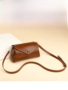 Detail view of smooth oil-wax leather texture and round buckle on a brown crossbody bag
