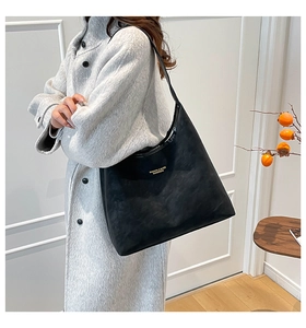 Détail du sac cabas en cuir mat noir avec logo doré et longue bandoulière sur mannequin