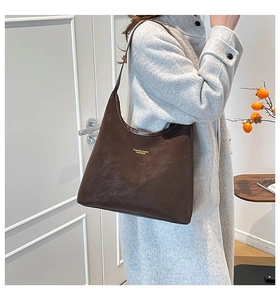 Détail du sac hobo marron foncé avec lettrage doré porté par un mannequin