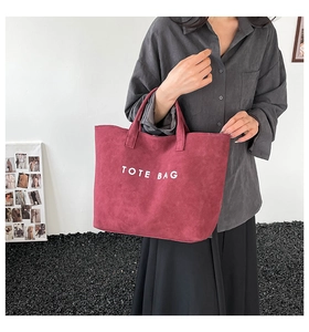 Detail of burgundy tote bag with white lettering held by a model in a minimal studio