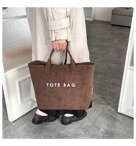 Detail of a large brown suede tote bag with white TOTE BAG lettering and dual handles