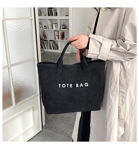 Detail of a large black tote bag with white text print held by a model in a modern room