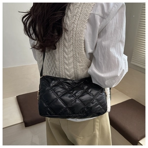 Detail of a black quilted crossbody bag with a diamond lattice pattern and soft texture