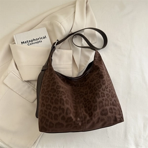 Fashionable leopard print hobo tote bag with brown leather strap on white blazer background