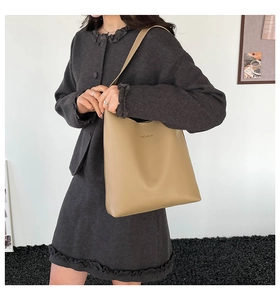 Detail of light brown leather tote bag with embossed Fashion logo on model's shoulder