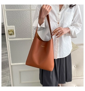 Close-up of brown leather tote bag with gold FASHION lettering worn on model shoulder
