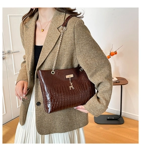 Detail of dark brown crocodile texture handbag with gold deer charm and chain strap
