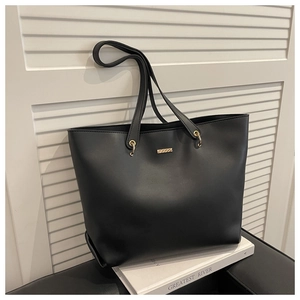 Détail d'un sac cabas noir minimaliste avec plaque en métal doré sur un livre