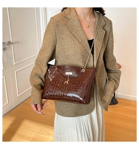 Detail of dark brown crocodile-embossed bucket bag with gold deer pendant and chain strap