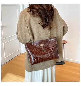 Detail view of brown crocodile texture shoulder bag with gold deer charm and chain strap