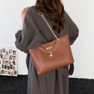 Brown faux crocodile leather tote bag with gold chain strap and deer charm on grey coat