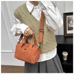 Detail of orange washed canvas handbag with adjustable strap and zip closure on side table