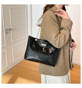 Detail view of black crocodile pattern tote bag featuring a gold deer charm and chain strap