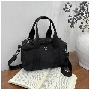 Detail of black canvas bag with metal M logo on an open book in a lifestyle setting
