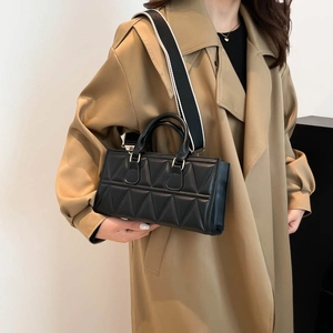 Modern black quilted handbag with wide striped strap worn over a khaki trench coat