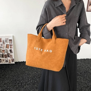 Large camel tote bag with TOTE BAG lettering being held by a model for a casual commute