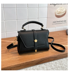 Close-up of black lychee grain leather handbag with gold hardware and vertical strap detail