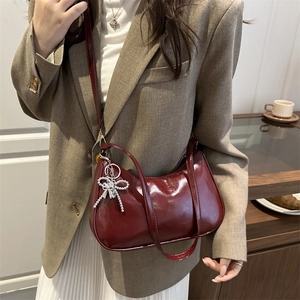 Glossy burgundy shoulder bag with silver strap and pearl bow charm in urban setting