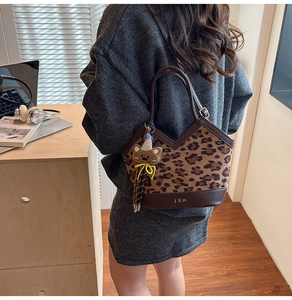 Close-up of leopard print suede handbag with leather trim and bear charm on a desk