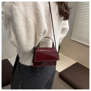 Detail of burgundy patent leather mini crossbody bag with high-gloss finish on a model
