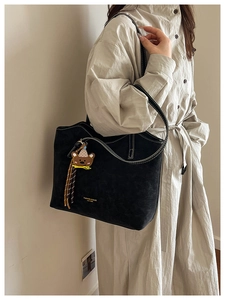 Detail of black matte leather tote bag featuring contrast white stitching and bear charm