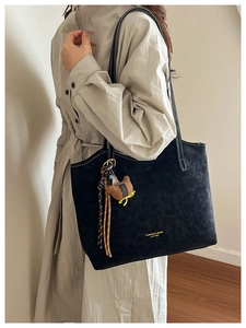 Close-up of black matte tote bag with white contrast stitching and plush animal charm