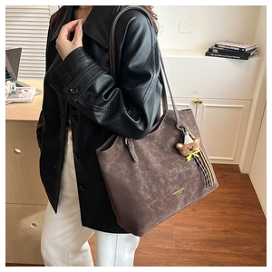 Close-up of a mocha brown tote bag with a bear charm and elegant leather texture