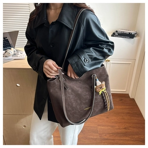 Detail of dark brown matte leather tote bag featuring fashion gold text and a bear charm