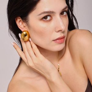 Überdimensionale goldene Halbkugel-Ohrstecker getragen von Model auf grauem Grund