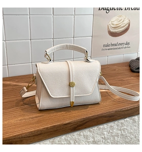 Close-up of cream pebble leather texture and gold circular buckle on a crossbody bag