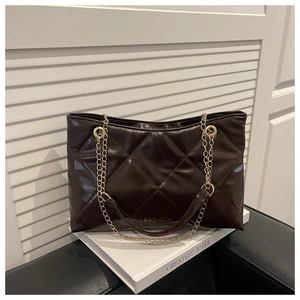 Détail d'un sac cabas matelassé marron foncé avec chaînes dorées sur livre blanc décor
