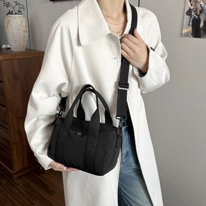 Minimalist black cylinder canvas crossbody bag with adjustable strap shown on model