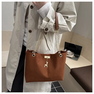 Détail d'un sac cabas en daim marron avec bandoulière chaîne dorée et pendentif cerf