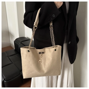Détail d'un cabas en daim beige avec bandoulière en chaîne dorée et pendentif cerf élégant