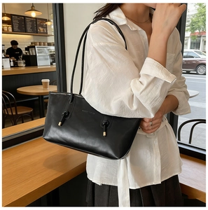 Detailed view of black leather shoulder bag with knot strap and gold metal hardware