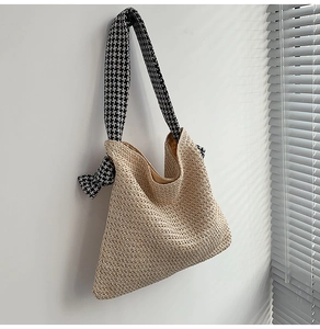 Detail of woven straw shoulder bag featuring a stylish black and white houndstooth strap