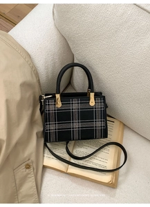 Detail of black plaid tote bag with cream stitching and gold hardware on vintage books