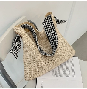 Close-up of straw tote bag featuring houndstooth ribbon handle and large decorative bow