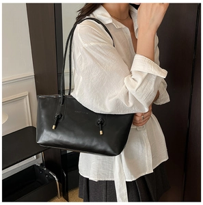 Detail view of black leather tote bag featuring gold hardware and shoulder strap knot